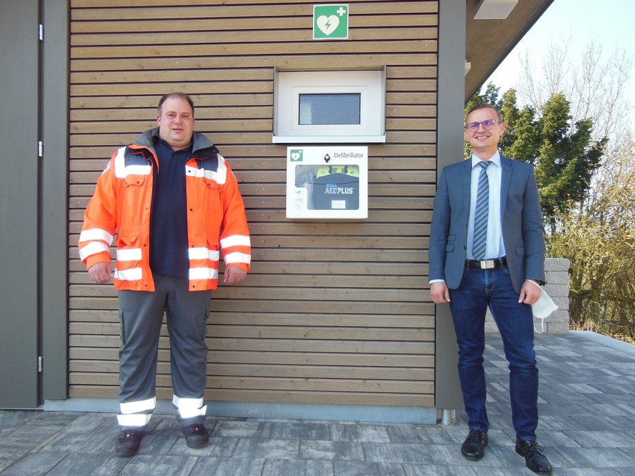 Bürgermeister Tobias Schneider und Jan-Kai Heller vom DRK-Ortsverein Rosenberg vor dem Defibrillator in Hohenberg